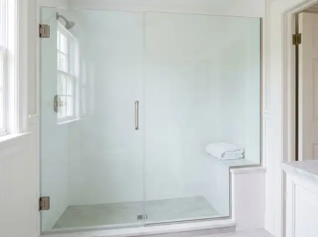 Frameless glass shower door closed against a white tiled shower